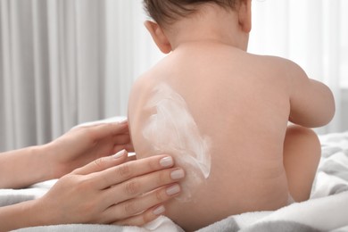 Photo of Mother applying body cream on her baby indoors, closeup