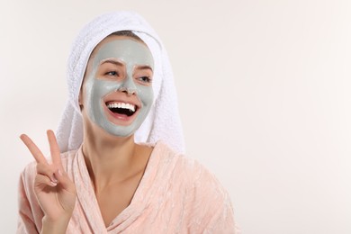 Woman with face mask showing v-sign on white background, space for text. Spa treatments