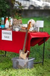 Paper with sign Garage sale and many different items on red tablecloth in yard