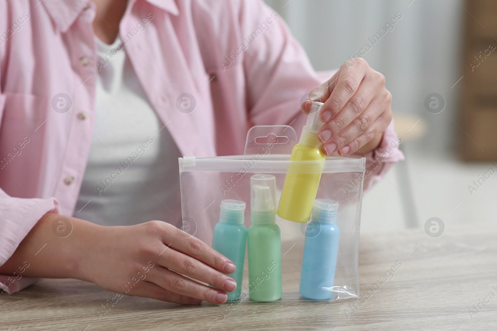 Photo of Woman packing cosmetic travel kit at wooden table indoors, closeup. Bath accessories