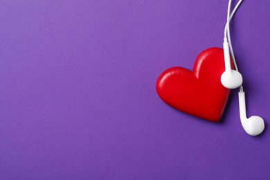 Photo of Modern earphones and red heart on purple background, flat lay with space for text. Listening love music songs