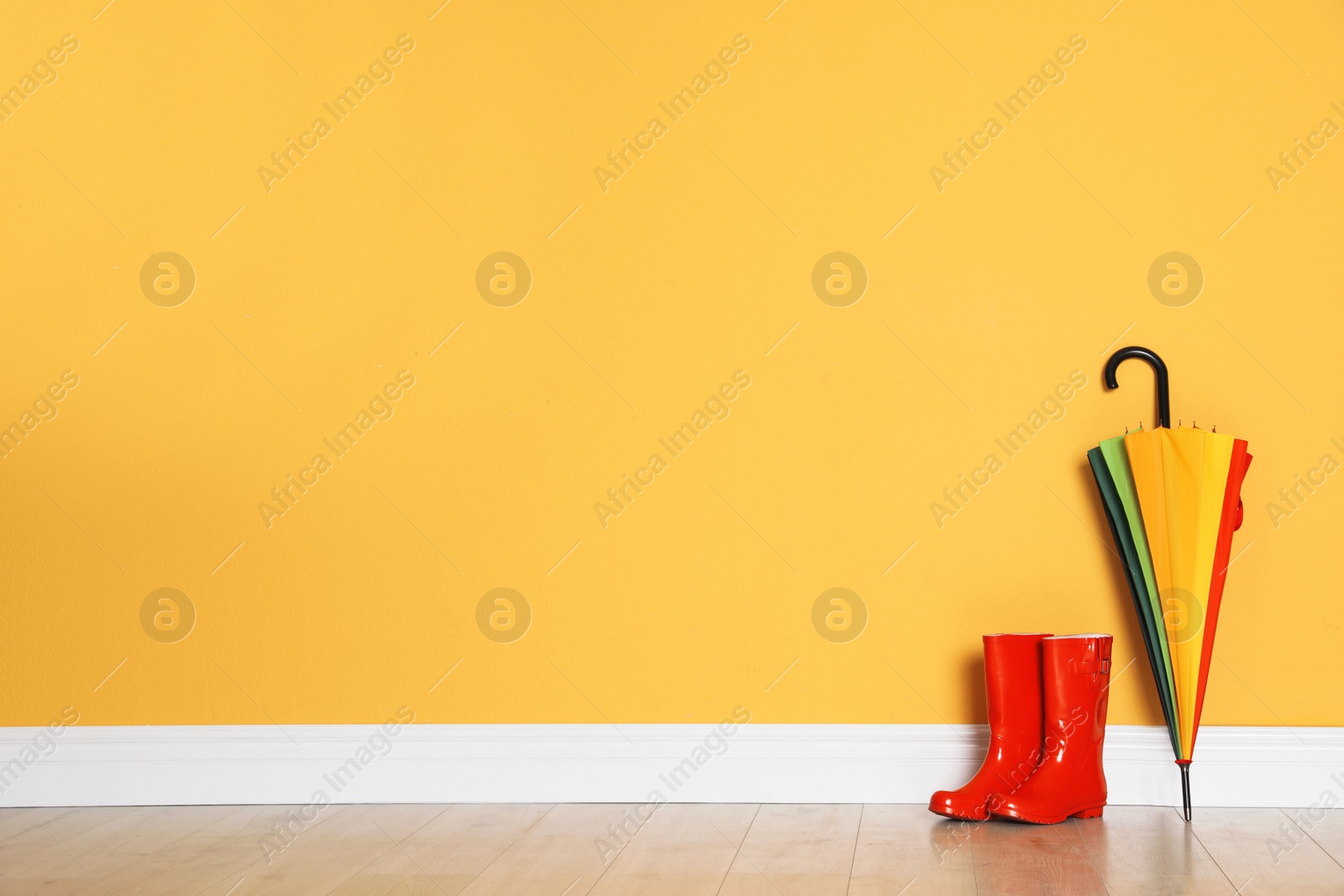 Photo of Beautiful umbrella and gumboots on floor near color wall with space for design