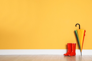 Beautiful umbrella and gumboots on floor near color wall with space for design