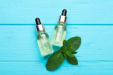 Photo of Bottles of essential oil and mint on turquoise wooden table, flat lay