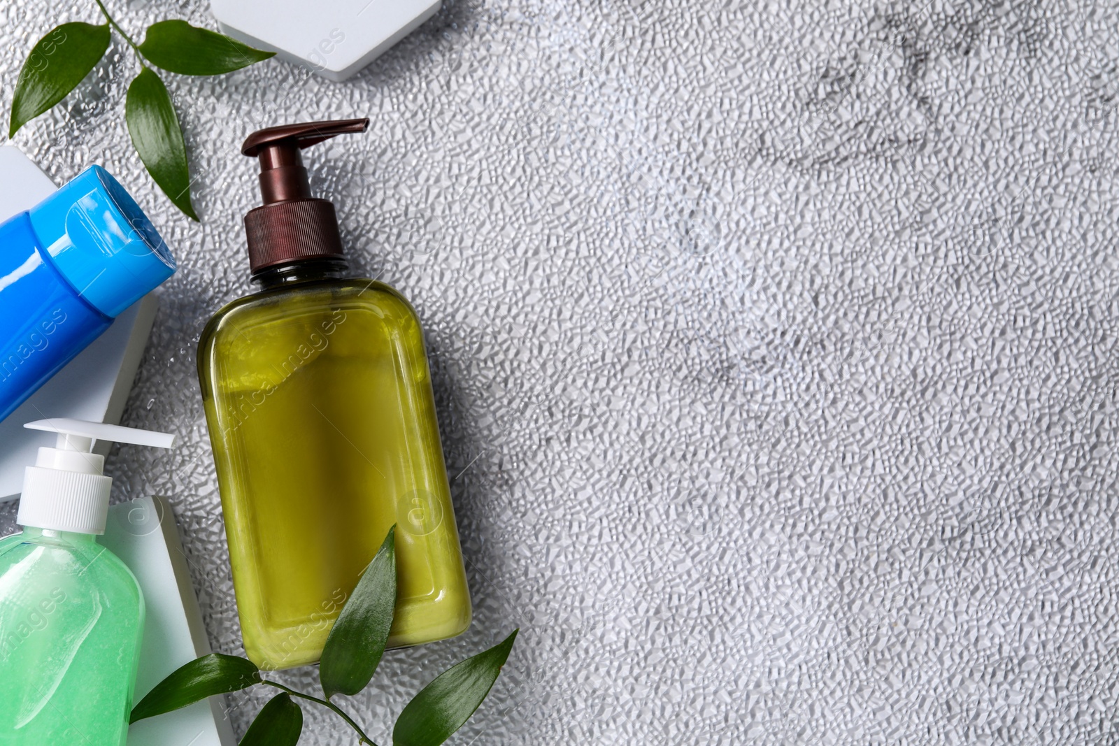 Photo of Different face cleansing products and green leaves on white textured table, flat lay. Space for text