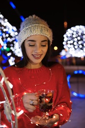 Woman with glass cup of mulled wine and garland at winter fair