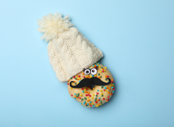 Photo of Funny face made with donut and knitted hat on light blue background, flat lay