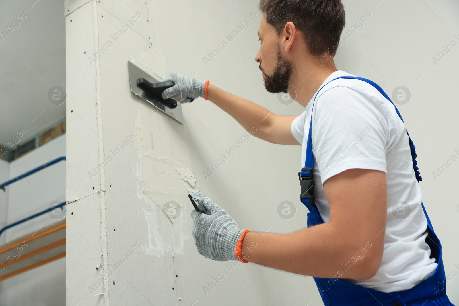 Photo of Professional worker plastering wall with putty knives indoors