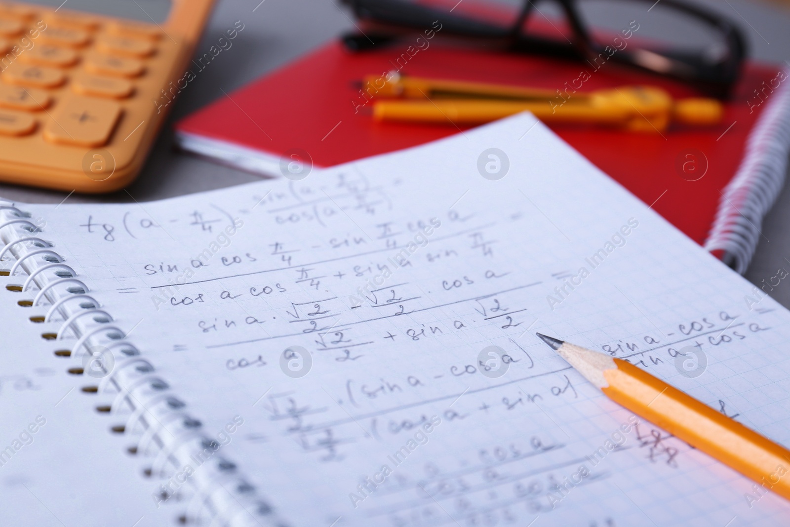 Photo of Notebook with homework and pencil on grey table, closeup