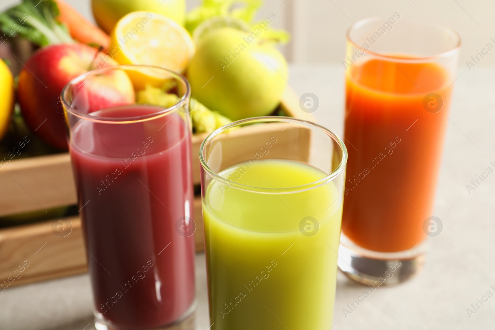 Photo of Glasses of different juices and wooden crate with fresh ingredients on table