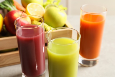 Glasses of different juices and wooden crate with fresh ingredients on table