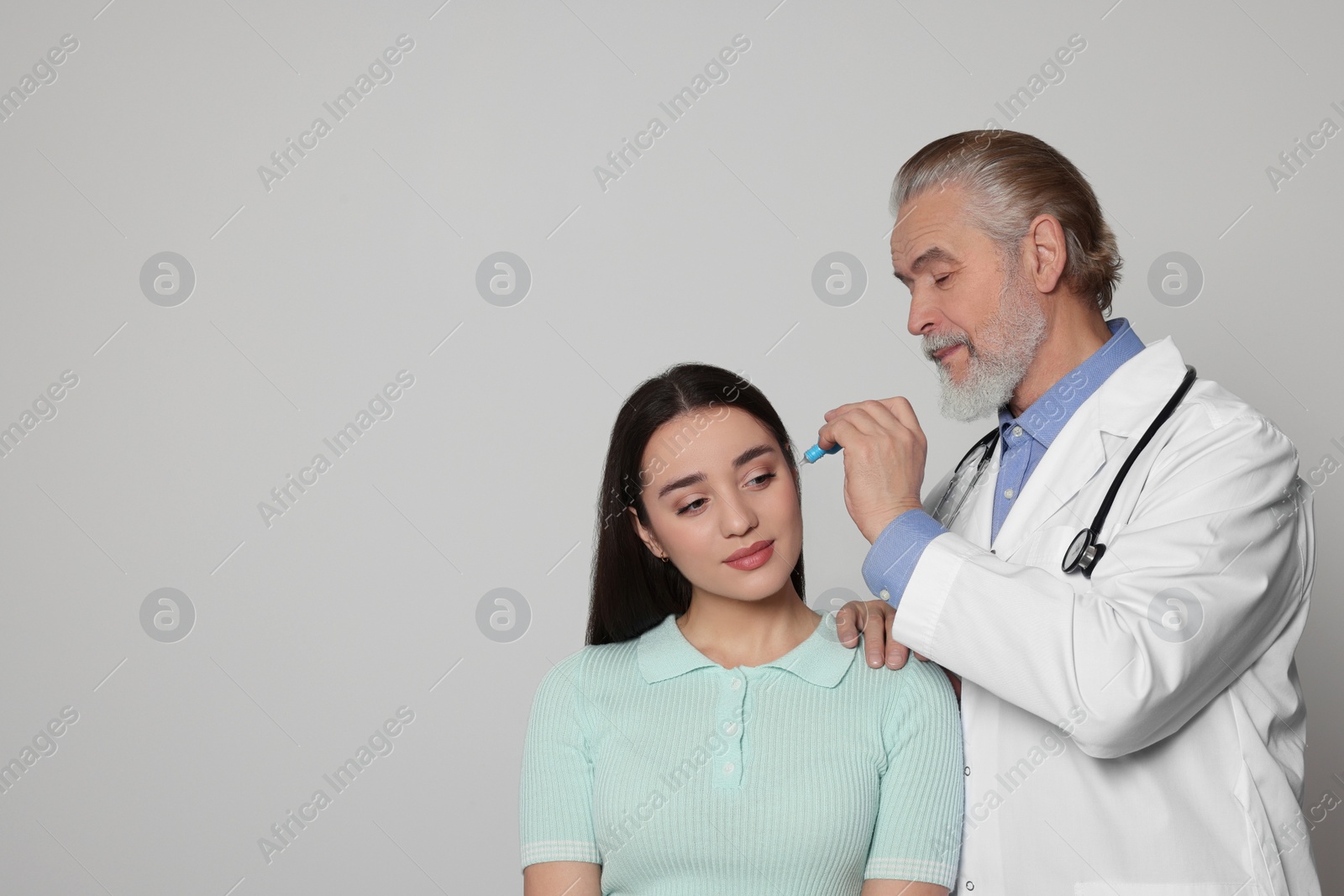 Photo of Doctor dripping medication into woman's ear on light grey background, space for text