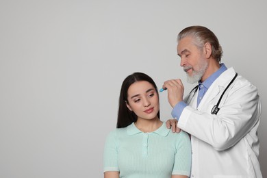 Doctor dripping medication into woman's ear on light grey background, space for text