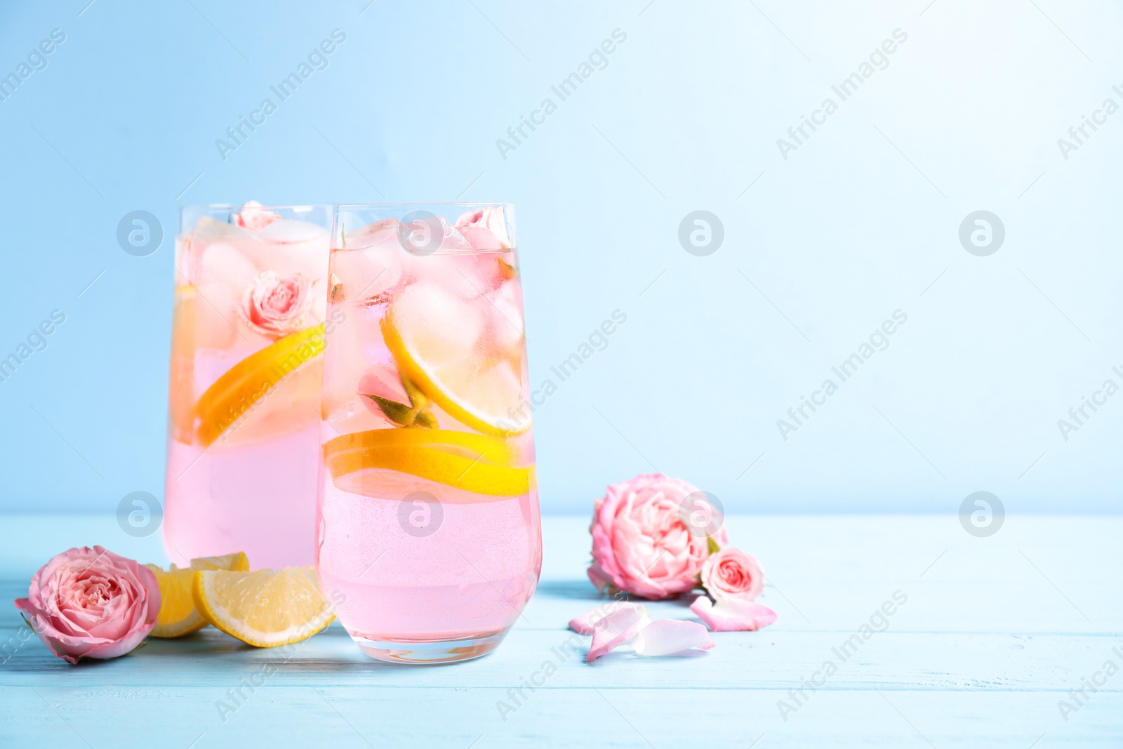 Photo of Tasty refreshing lemon drink with roses on wooden table against light blue background. Space for text