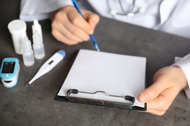 Photo of Doctor writing at table with different medical objects, closeup with space for text