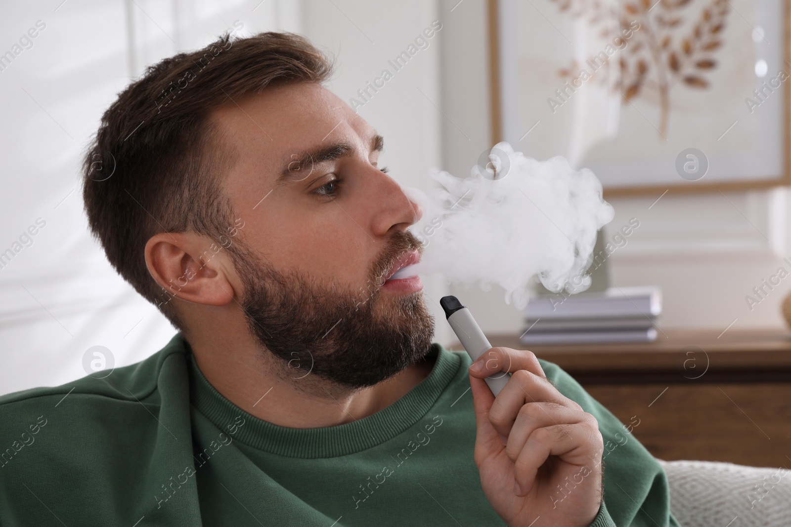 Photo of Handsome young man using disposable electronic cigarette at home
