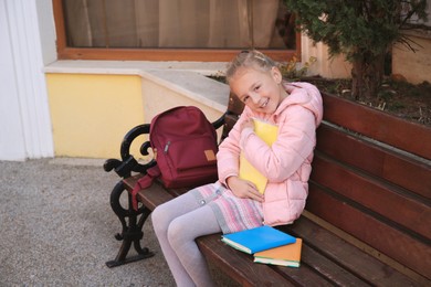Cute little girl with backpack and books on bench outdoors. Space for text