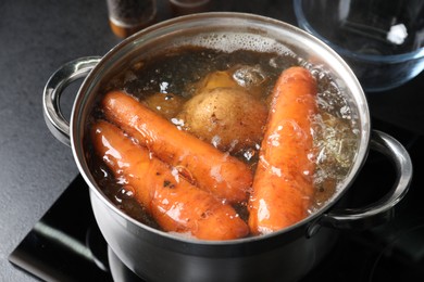 Photo of Boiling carrot and potatoes in pot on electric stove, closeup. Cooking vinaigrette salad