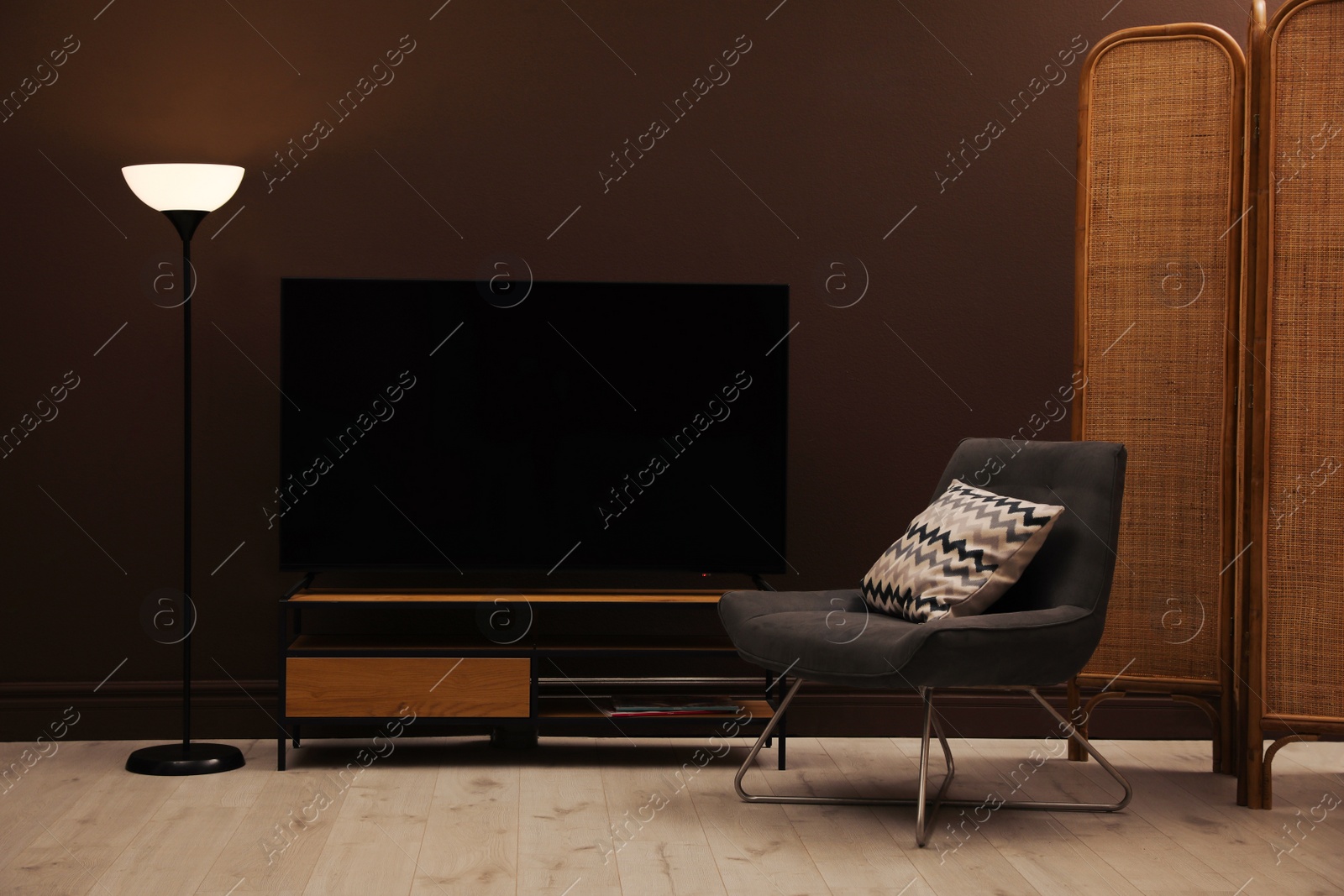 Photo of Modern TV on cabinet, armchair and floor lamp near brown wall in room. Interior design