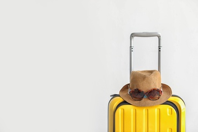 Photo of Bright yellow suitcase with hat and sunglasses on light background