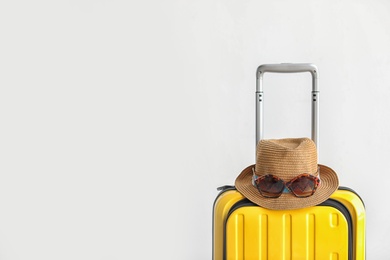 Bright yellow suitcase with hat and sunglasses on light background