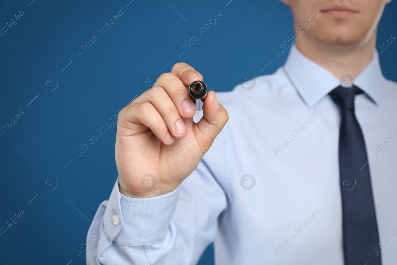 Photo of Businessman with marker against blue background, focus on hand