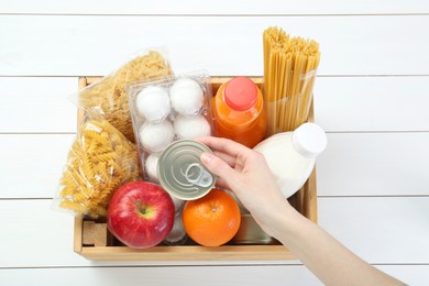 Photo of Humanitarian aid. Woman with food products for donation at white wooden table, top view