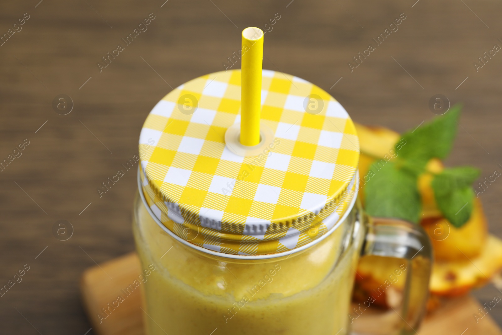 Photo of Tasty pineapple smoothie in jar, mint and sliced fruit on wooden table, closeup