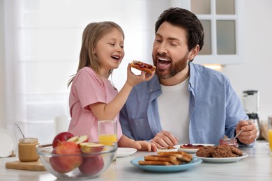 Father and his cute little daughter having breakfast at table in kitchen