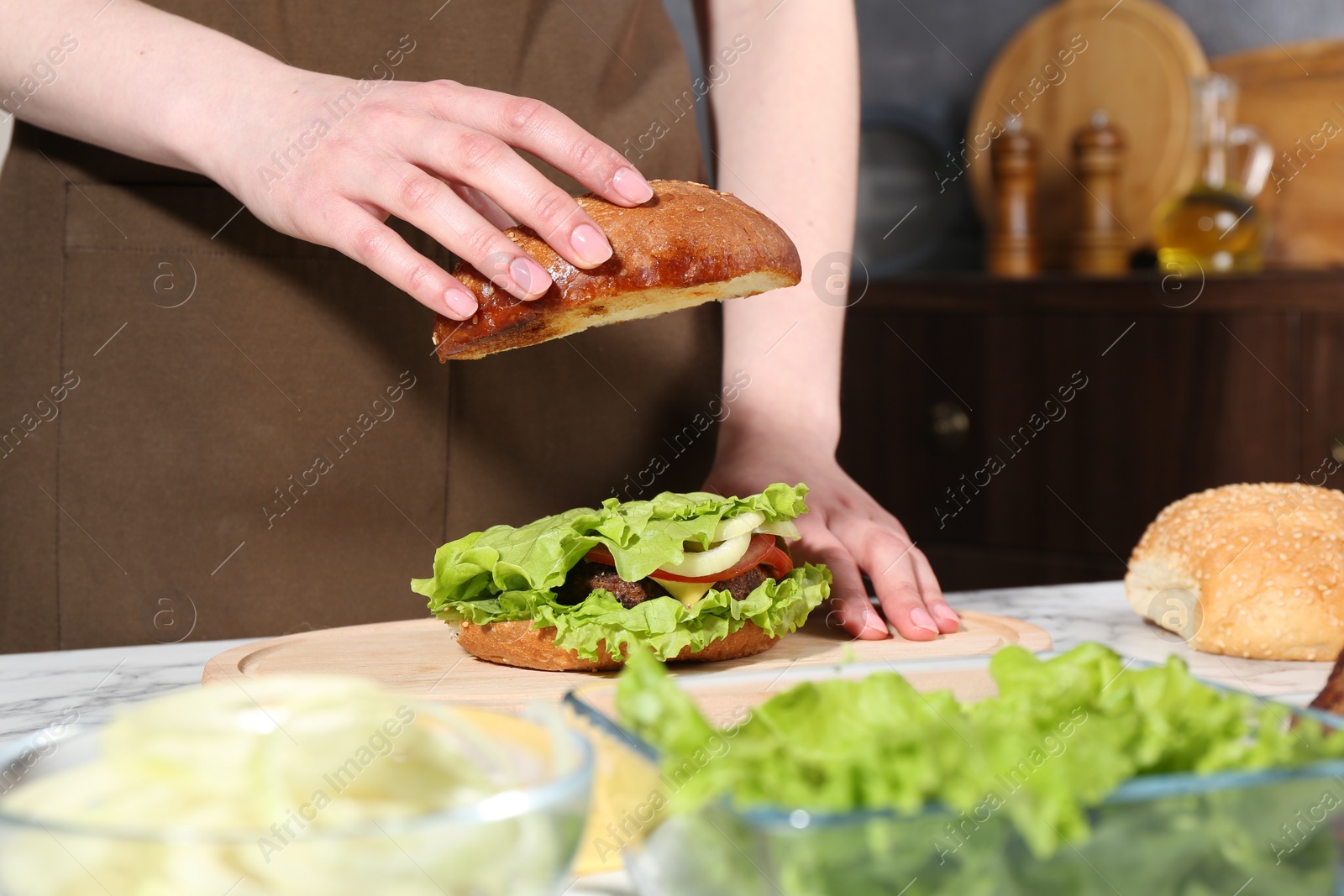 Photo of Woman making delicious vegetarian burger at white marble table, closeup