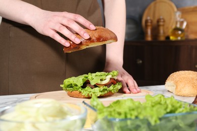 Woman making delicious vegetarian burger at white marble table, closeup