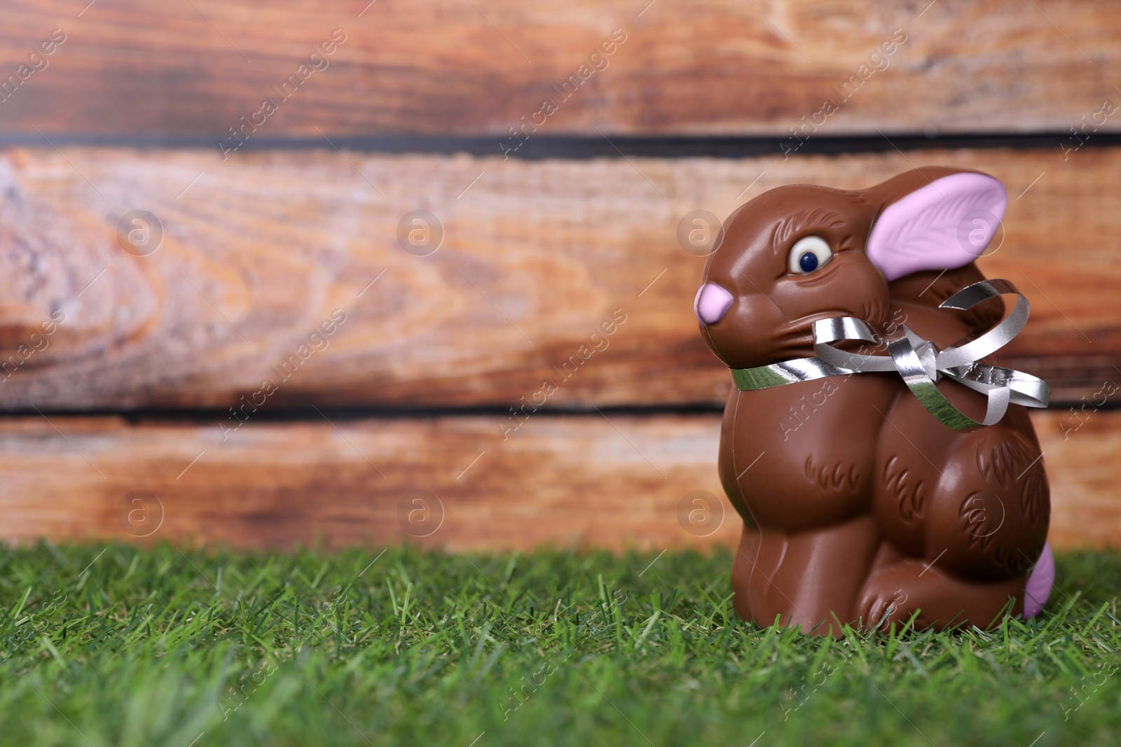 Photo of Easter celebration. Cute chocolate bunny on grass against wooden background. Space for text