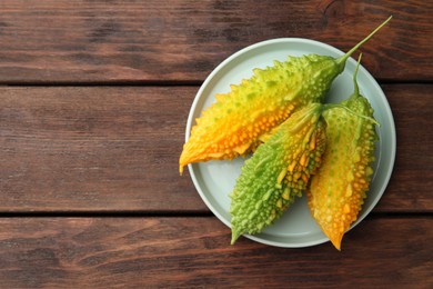 Photo of Plate with fresh bitter melons on wooden table, top view. Space for text