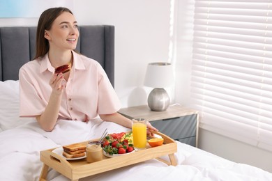 Smiling woman having breakfast in bed at home. Space for text