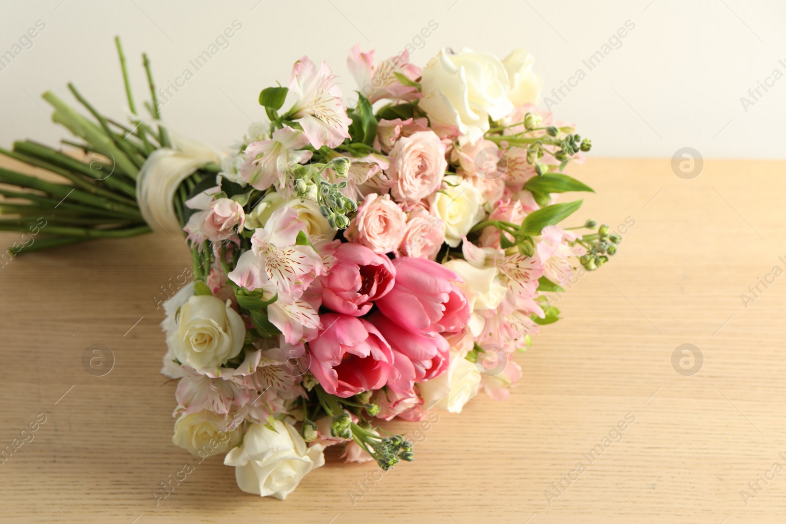 Photo of Beautiful bouquet of fresh flowers on wooden table near light wall