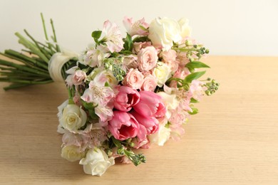 Beautiful bouquet of fresh flowers on wooden table near light wall