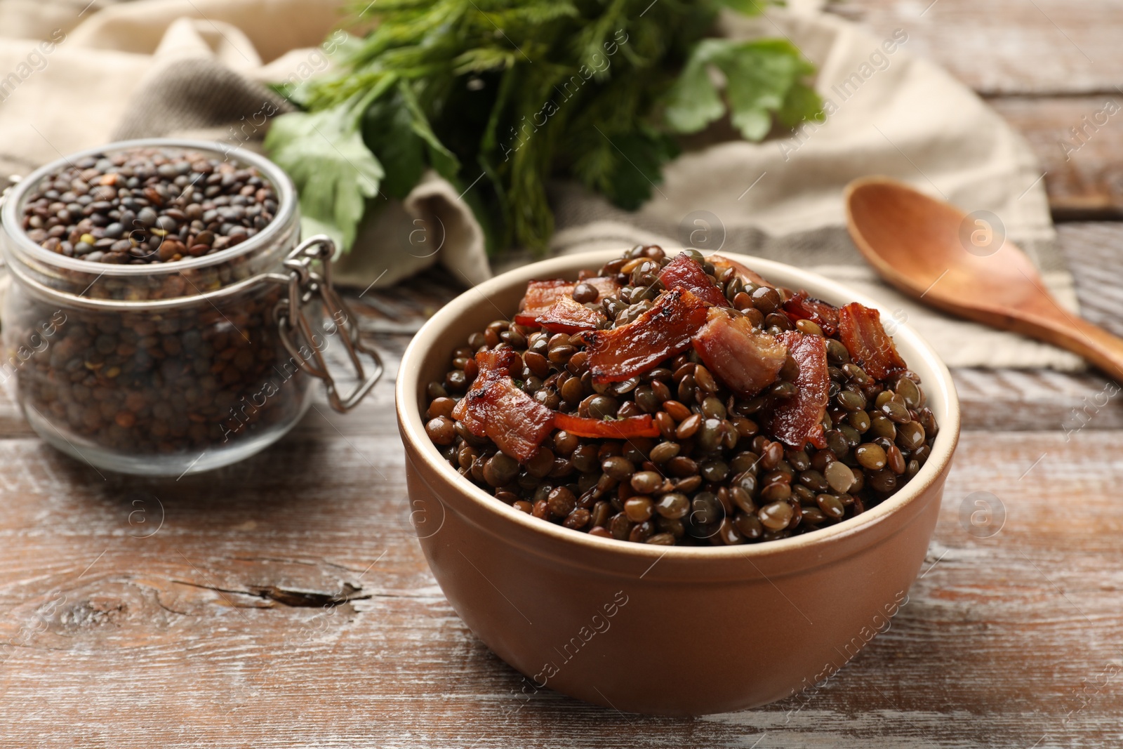 Photo of Delicious lentils with bacon in bowl on wooden table, closeup