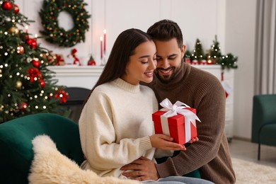 Photo of Beautiful young couple with Christmas gift at home