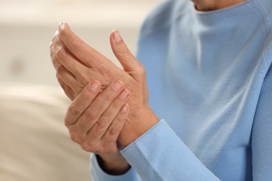 Mature woman suffering from pain in hand indoors, closeup. Rheumatism symptom