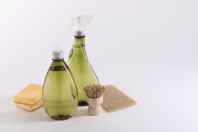 Photo of Bottles of cleaning product, brush and sponges on white background