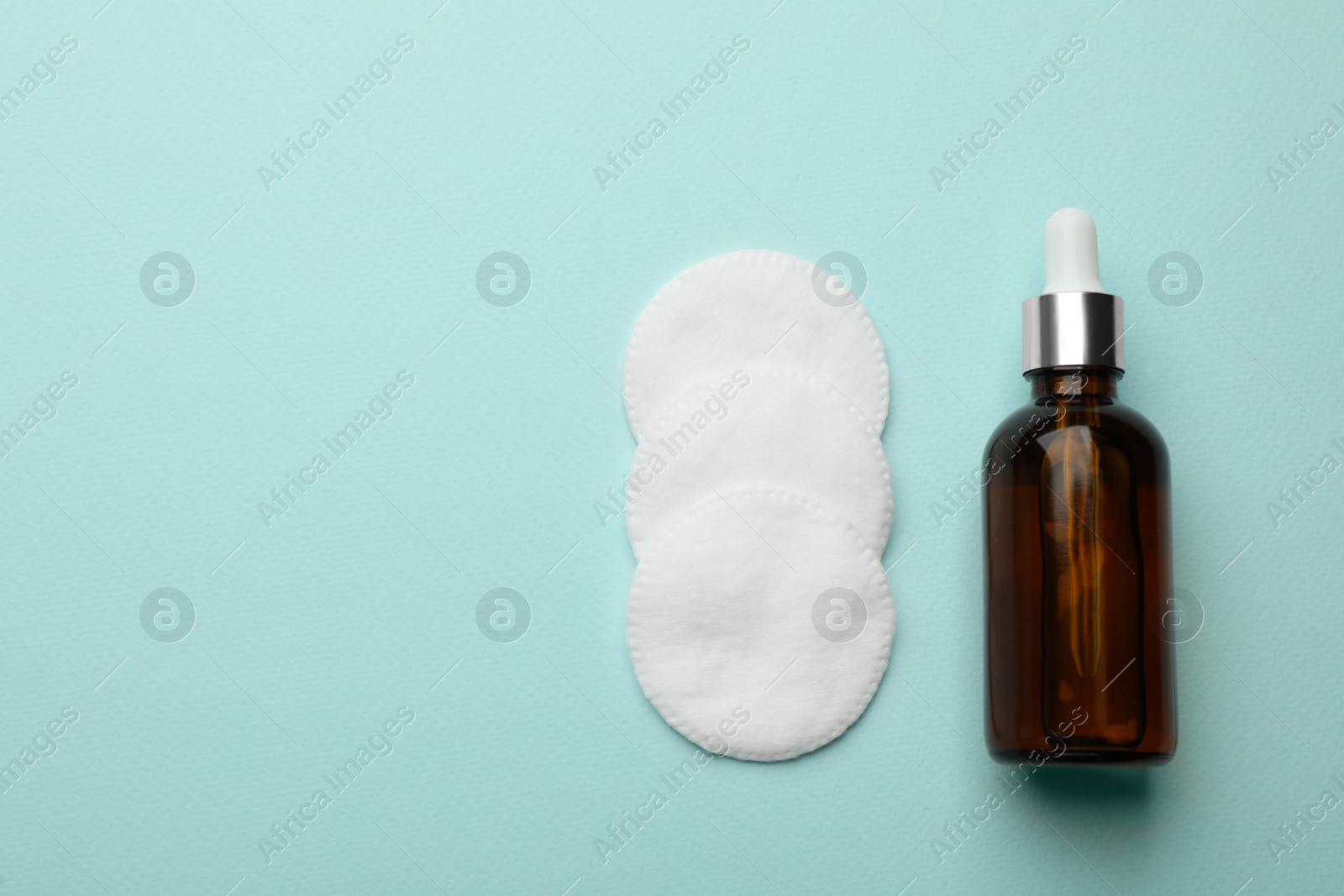 Photo of Cotton pads and makeup removal product on light blue background, flat lay. Space for text