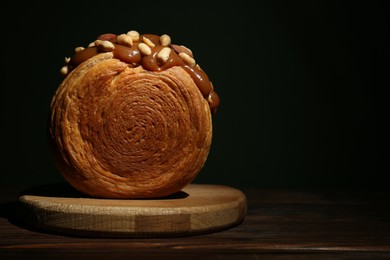 Photo of Round croissant with chocolate paste and nuts on wooden table, space for text. Tasty puff pastry