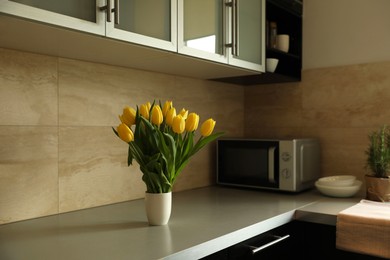 Photo of Bouquet of beautiful yellow tulips on countertop in kitchen, space for text