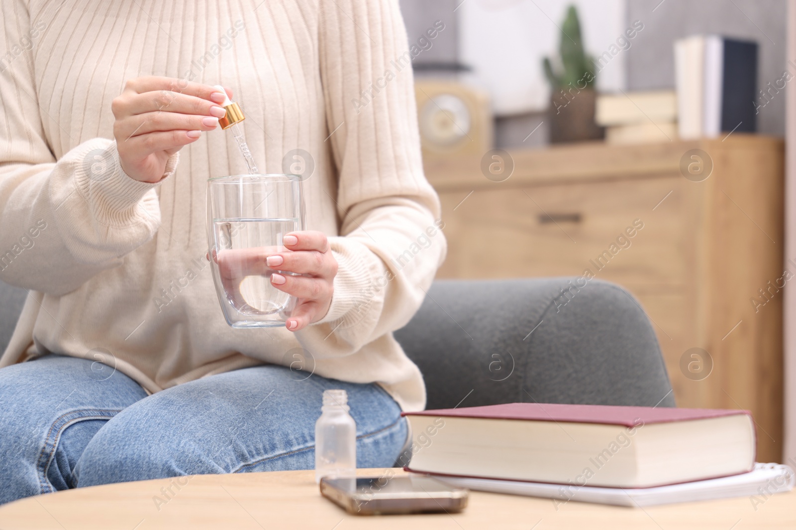 Photo of Woman dripping food supplement into glass of water on wooden table indoors, closeup