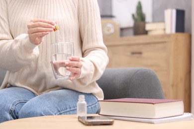 Photo of Woman dripping food supplement into glass of water on wooden table indoors, closeup