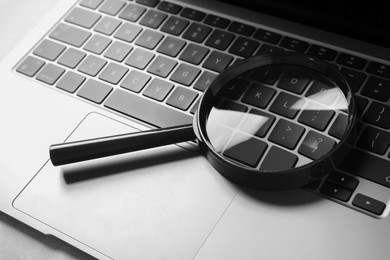 Photo of Magnifying glass and laptop on light grey table, closeup