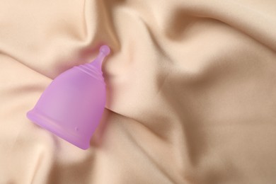 Photo of Menstrual cup on beige silk fabric, top view. Space for text