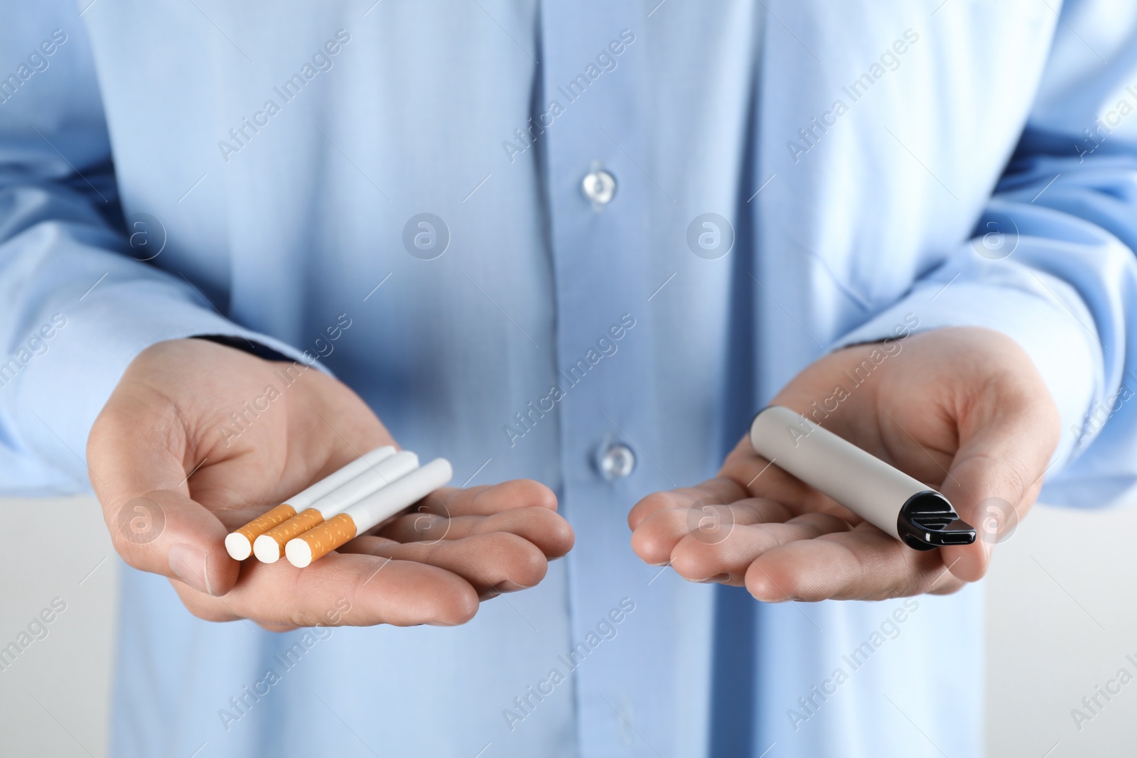 Photo of Man with cigarettes and vaping device on light background, closeup. Smoking alternative