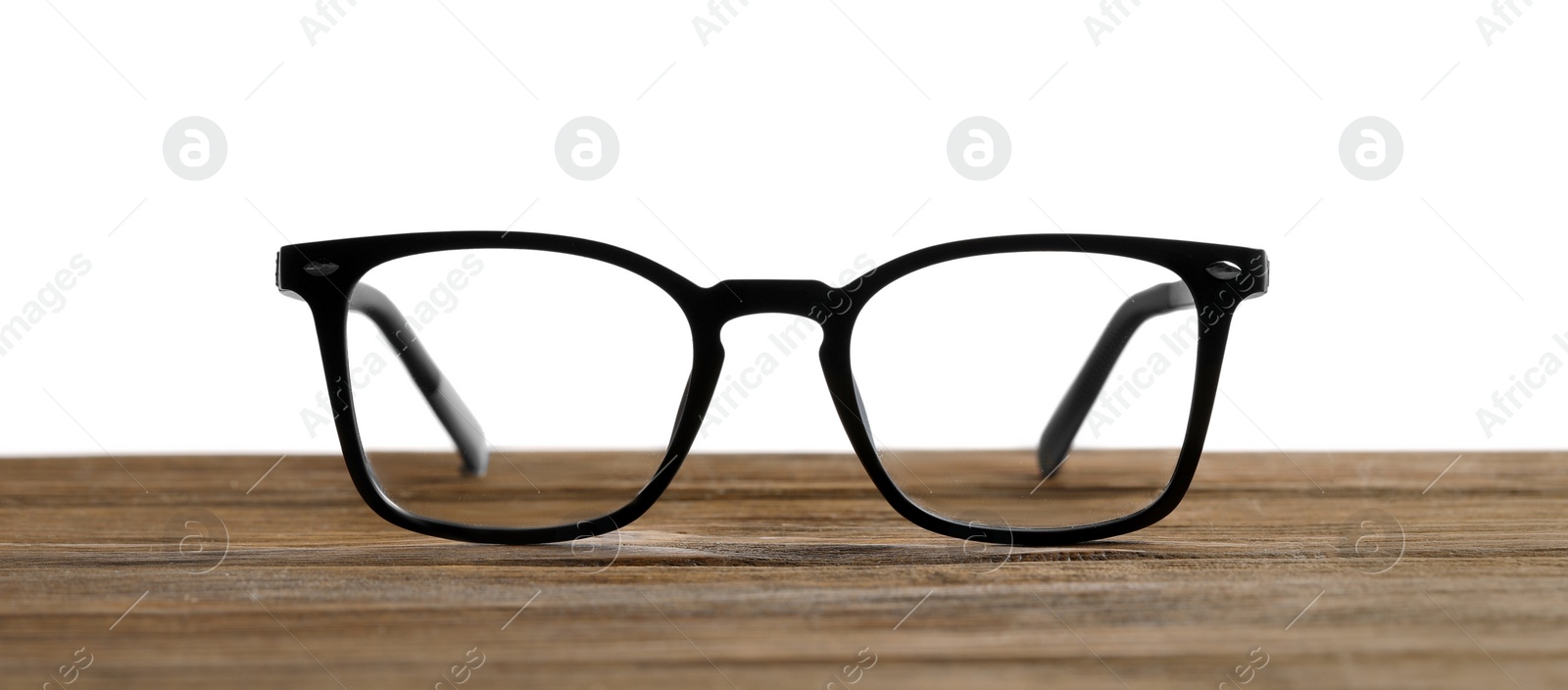 Photo of Stylish glasses with black frame on wooden table against white background