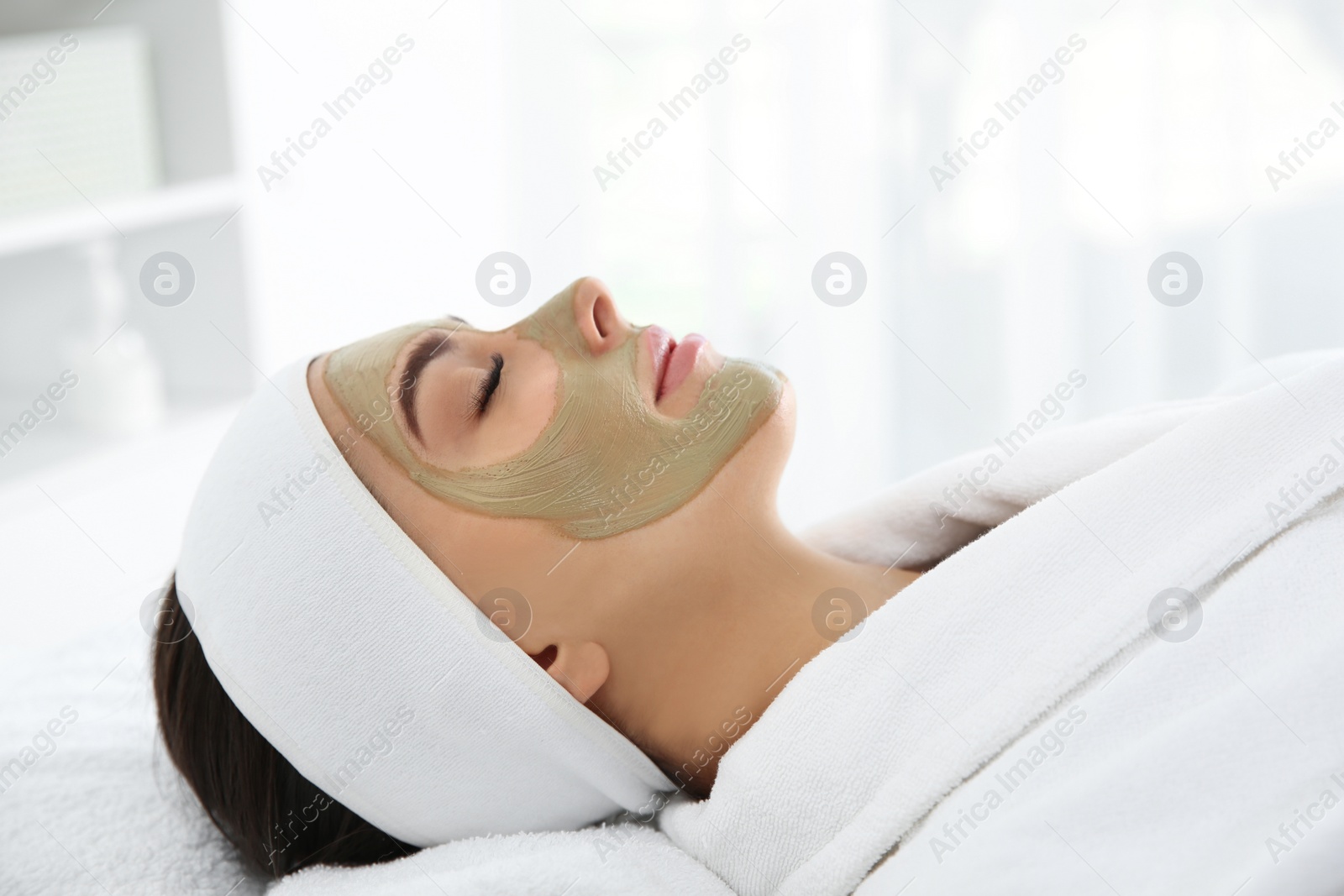 Photo of Pretty woman with clay mask on her face in spa salon